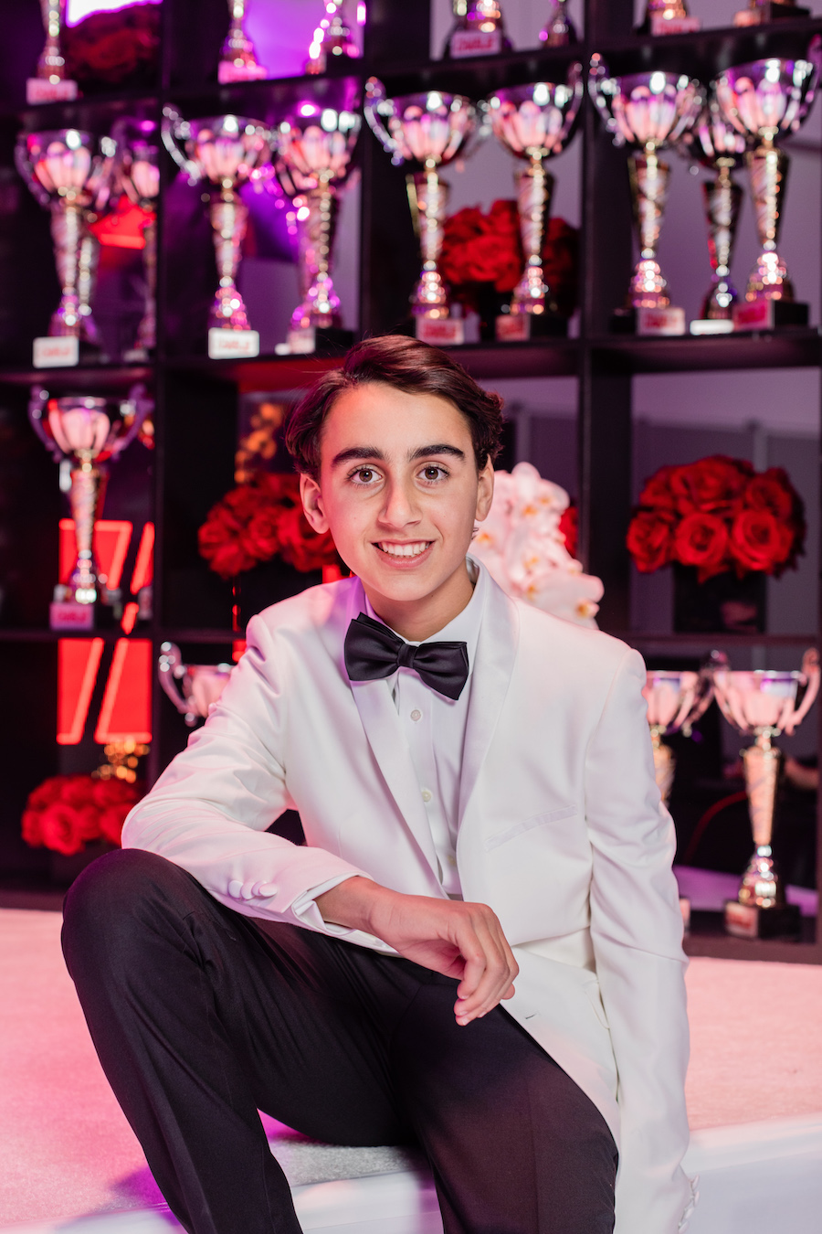 boy smiling with trophies and red rose bouquets in the background at bar mitzvah